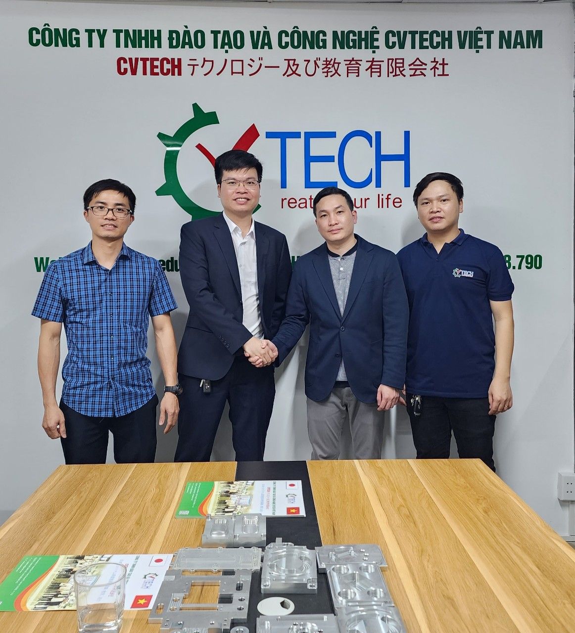 Bốn người đứng chụp ảnh trước phông logo CVTECH, bàn có sản phẩm mẫu - pmttgroup gặp mặt học viên cvtech