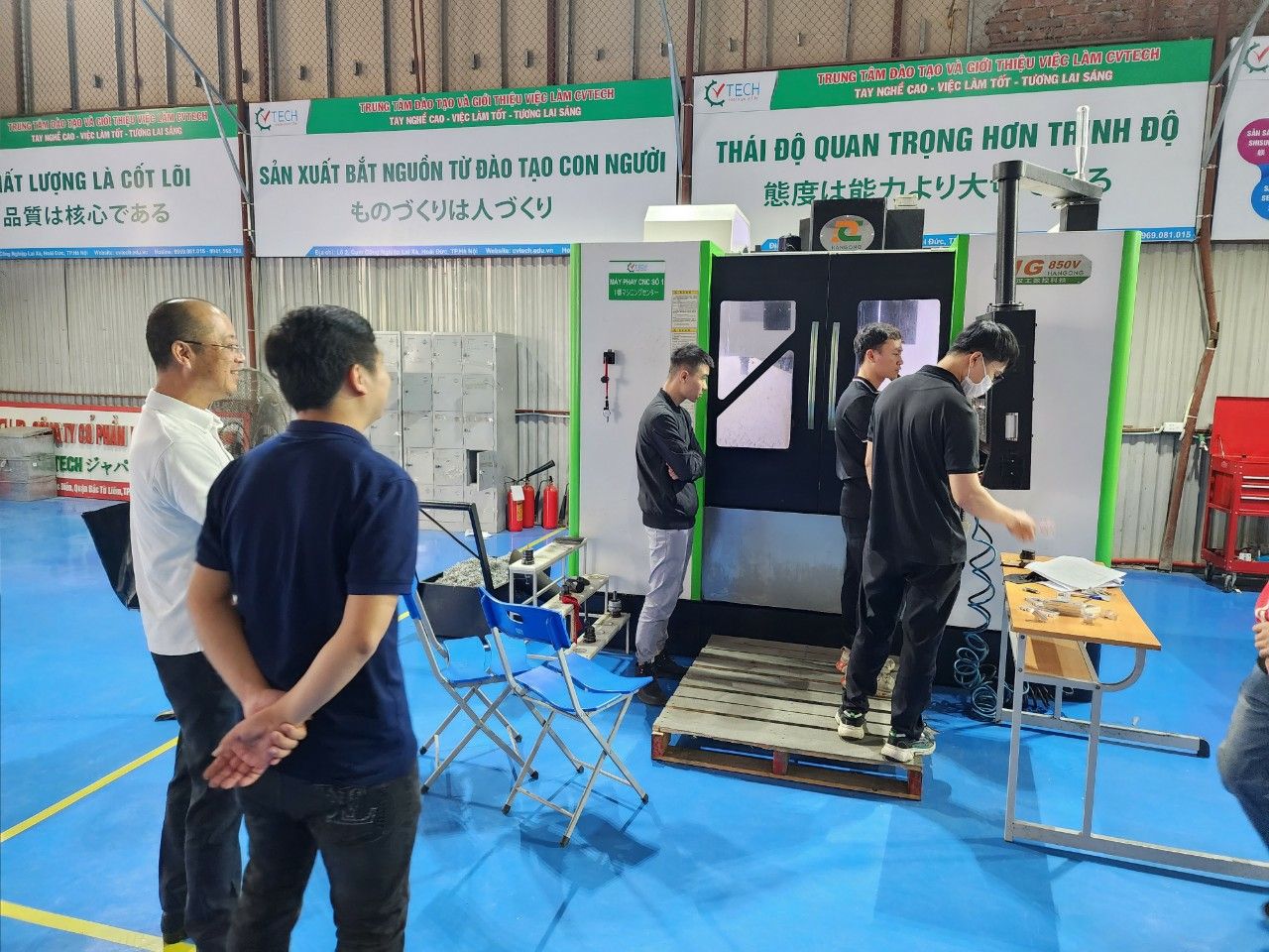 Giảng viên và học viên đứng trước máy phay CNC trong buồng kính - học nghề gia công cnc