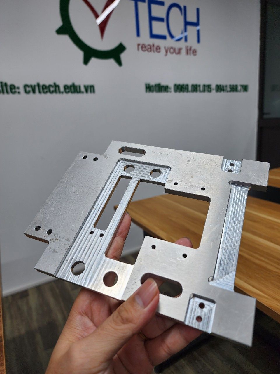 Tấm nhôm gia công nhiều lỗ cầm trên tay trước phông logo CVTECH - gia công cơ khí cnc