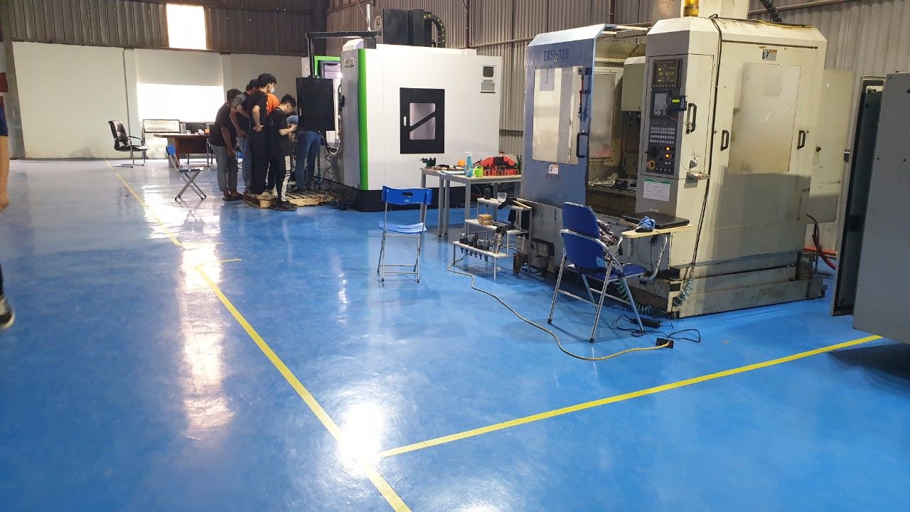 Xưởng thực hành với máy phay CNC cỡ lớn bên trái và dãy phòng học kính phía sau - chuẩn bị máy phay cnc