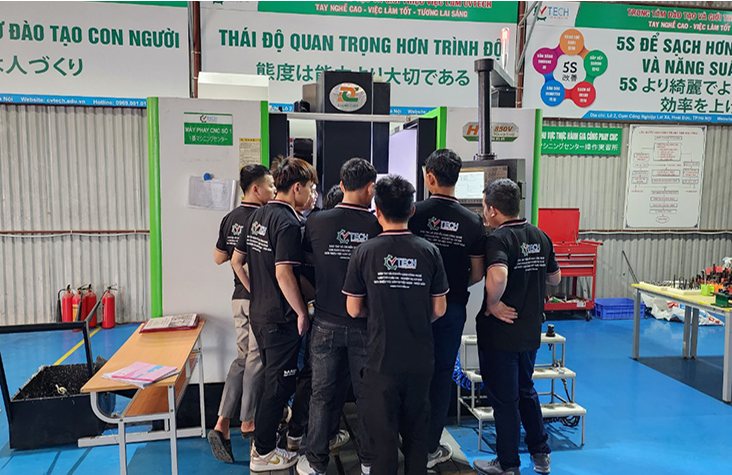 Nhóm học viên đứng quanh máy CNC trong xưởng